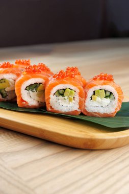 Somon, salatalık ve avokado ile dolu taze suşi ruloları ahşap servis tabağında oturur. Parlak turuncu somon ve malzemeler yemeğe renk katar..