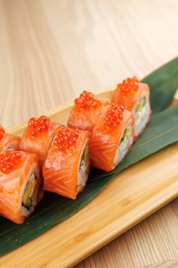 Taze somon ve canlı yumurtayla kaplı suşi ruloları, ahşap bir tabakta bambu yaprağıyla sunuluyor..