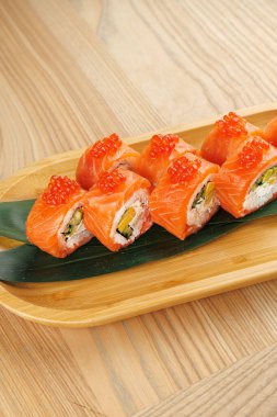 Somon, avokado ve havyardan yapılan taze suşi ruloları ahşap bir tabakta sunulur. Bu yemek malzemelerin canlı renklerini ve dokularını gösteriyor..