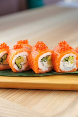 Balık yumurtası ile kaplı taze somon ve avokado içeren suşi dürümleri öğle yemeği saatinde ahşap bir tabakta düzenlenmiştir..