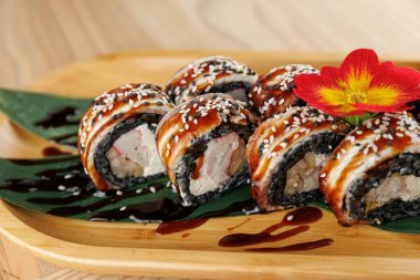 Ahşap bir tabağa yerleştirilmiş yengeç ve krem peynirle dolu suşi ruloları. Ekmekler sosla kaplanır ve çiçeklerle süslenir. Bu da davetkar bir yemek yaratır..