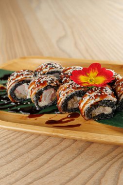 Pirinç, deniz yosunu ve çeşitli dolgulardan yapılan suşi ruloları bambu tabağında güzelce sıralanır. Renkli bir çiçek tabağa dekoratif bir dokunuş ekler..