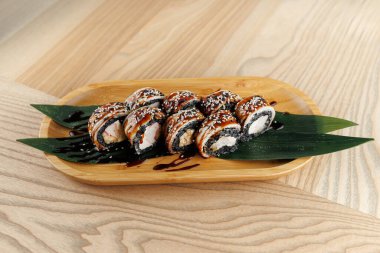 Tahta bir tabakta taze suşi ruloları var. İçi malzemelerle dolu ve susam tohumlarıyla kaplı. Yeşil yapraklar biraz renk katar. Bu yemek Japon mutfağında enfes bir deneyim sunuyor..