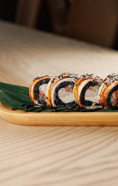 Balık ve pirinçle dolu suşi ruloları bambu yaprağıyla ahşap bir tabakta düzgünce düzenlenir. Masa yüzeyi hafif ahşap, basit bir yemek atmosferi yaratıyor..