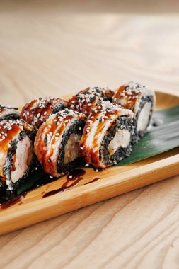 Çeşitli suşi ruloları ahşap bir tabağa düzgünce yerleştirilir. Ekmekte yosunlara sarılmış, soslu ve susamlı malzemeler yer alıyor. Ayar gündelik ve davetkar..