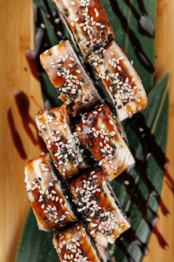 Suşi ruloları bambu yaprakları üzerinde güzelce düzenlenir. Her rulo susam tohumuyla kaplanmış ve lezzetli bir sos serpiştirilmiş. Bu yemek lezzet ve dokuların karışımını sergiliyor, suşi severler için mükemmel..