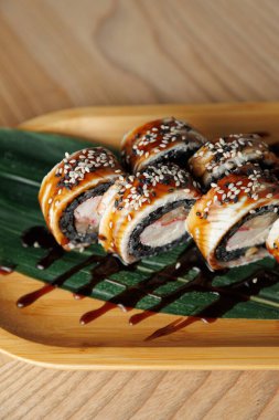 Suşi ruloları suşi pilavı, yosun ve balıklar ahşap bir tabakta düzenlenir. Ekmekler susam tohumlarıyla kaplı ve bir restoranda suşi sosu serpiştirilmiş..