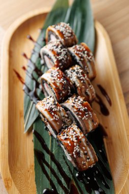 Tahta bir tabakta suşi ruloları sergilenir. Yılanbalığı ile doldurulur ve susam tohumlarıyla süslenir. Ekmekler muz yapraklarının üzerine serpiştirilip renkli bir sunum yaratıyor..