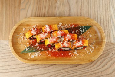 Suşi ruloları, üzerine yengeç sosu, yumurta şeritleri ve üzerine pirinç serpiştirilmiş ahşap bir tabağa konur. Bu yemek, doğal ahşap atmosferi olan bir restoranda hazırlandı..