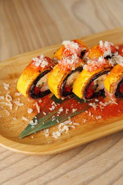 Birkaç canlı suşi rulosu ahşap bir tabakta sergilenir. Her rulo titizlikle baharatlı gevrekler ve doğranmış soğanlarla süslenmiş..