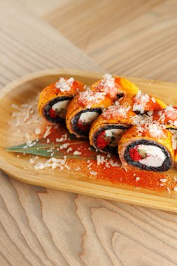 Ahşap tabakta krema, yengeç ve renkli malzemelerle dolu suşi ruloları var. Zarif rendelenmiş peynir ve baharatlar Japon mutfağını süslüyor..