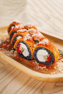 Krem peynir, sebze ve baharatla dolu suşi ruloları köy restoranındaki ahşap bir tabağa konur. Ekmeğin canlı renkleri ve eşsiz bir sunumu var..
