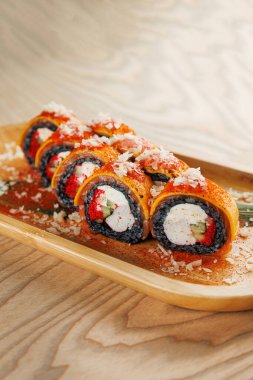 Suşi börekleri yengeç, salatalık ve baharatlı sos gibi çeşitli malzemeler içerir. Ahşap bir tabakta servis edilir, malzemelerle süslenir, yemek için mükemmeldir..