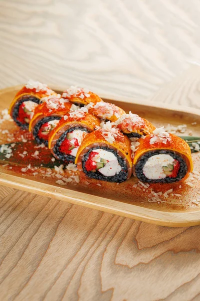 Ahşap bir tabakta sebze ve krem peynirle dolu ve malzemelerle süslenmiş çok sayıda canlı suşi ruloları yer alıyor. Yemek sırasında keyif almak için güzelce düzenlenir..