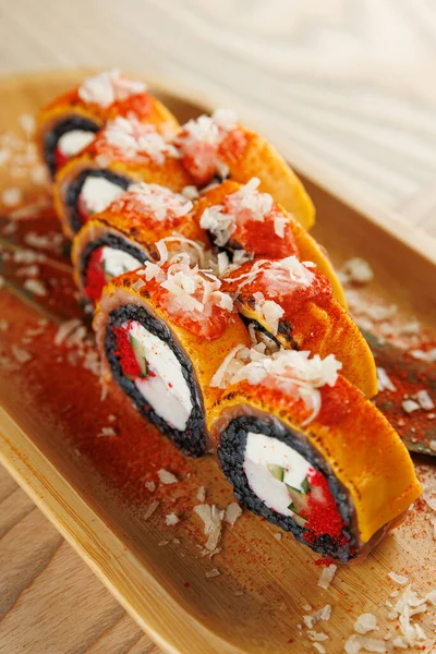 Ahşap bir tabakta sergilenen suşi rulolarının bir seçimi canlı renkler ve çeşitli malzemeler, mutfak geleneklerinin kaynaşmasını vurguluyor..