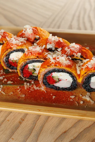 Krem peynir, sebze ve dilimlenmiş deniz ürünleri ve baharatlarla dolu suşi ruloları bir restoran masasında ahşap bir tabakta sunuluyor..