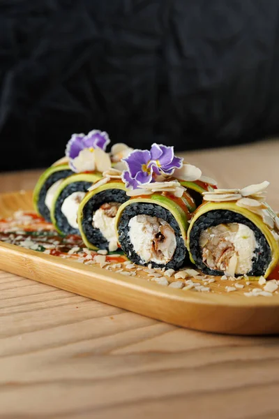 Suşi ruloları ahşap bir tabakta güzelce düzenlenir. İçinde çiçekler ve fındıkla süslenmiş avokado ve balık gibi malzemeler var. Lezzetli bir Japon yemeği..