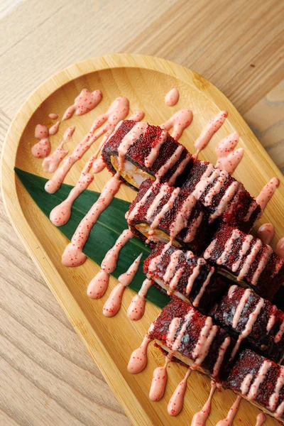 Suşi ruloları bambu tabakta güzelce düzenlenir. Ekmeğin üzerine canlı pembe bir sos serpiştirildi. Ortam gündelik ve davetkar, arkadaşlarla yemek yemek için mükemmel..