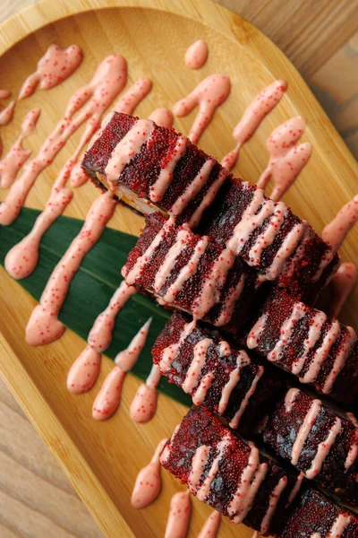 Suşi ruloları ahşap bir tabakta güzelce düzenlenir, pembe soslu katmanlar ve renkler sergilenir. Yemek, suşi yapma ve sunum becerisini vurguluyor..