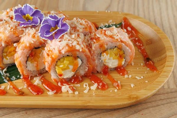 Suşi ruloları ahşap bir tabakta güzelce düzenlenir. Tabakta çiçekler ve soslar da dahil olmak üzere canlı malzemeler yer alıyor..