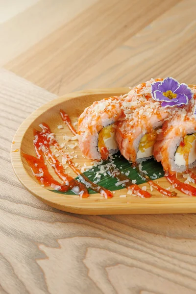 Suşi ruloları ahşap bir tabağa konur, sos ve çiçekle süslenir. Renkli malzemeler masanın üzerinde lezzet ve dokuların bir karışımını sergiler..