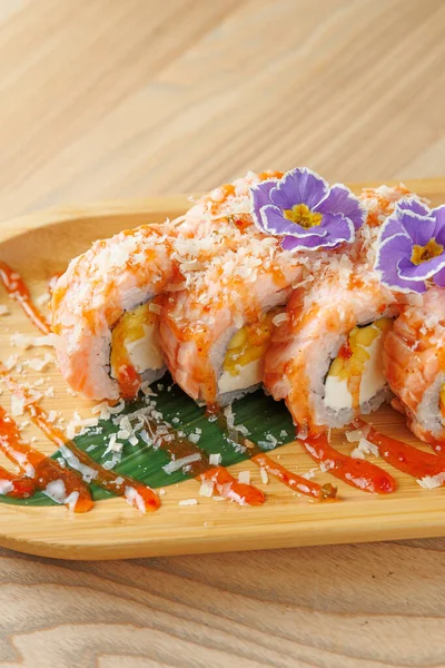 Suşi ruloları ahşap bir tabakta sergilenir, çiçek gibi süslerle kaplanır, sosla ıslatılır, ve restoran ortamında servis edilir,.
