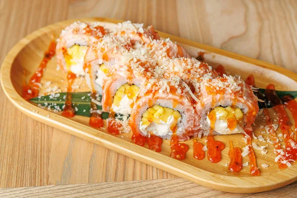 Suşi ruloları ahşap bir tabağa konur. Ekmekler renkli soslar ve süslemelerle kaplı. Arka planda sıcak bir yemek ortamı var. Japon mutfağından zevk almak için mükemmel..