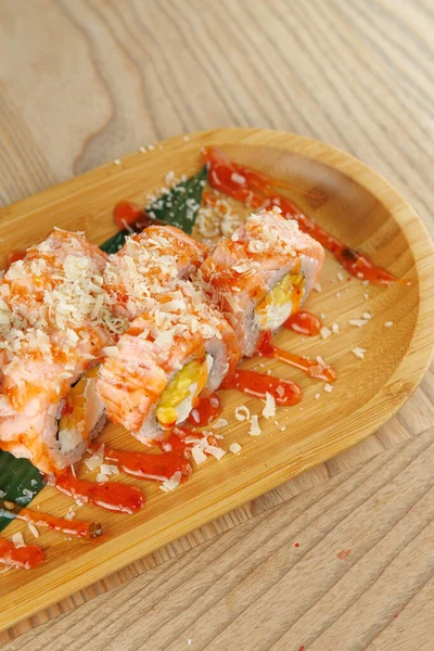 Suşi ruloları domates sosu ve malzemelerle ahşap bir tabağa konur. Dekor parlak, tabakları aydınlatıyor. Bu yemek Japon mutfağının özünü yansıtıyor..