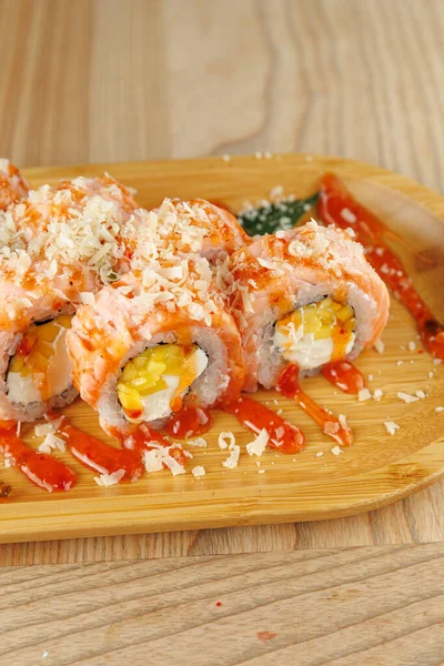 Suşi dürümleri ahşap bir tabakta servis edilir. Baharatlı sos ve çıtır çıtır gevreklerle süslenmiş balık ve dolgu tabaklarıyla lezzetli bir yemek için..