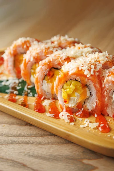 Yengeç ve yumurta katmanlı suşi ruloları ahşap bir tabakta sunulur. Tabakta üzerine serpiştirilmiş soslar ve bir garnitür balık gevreği yer alıyor..