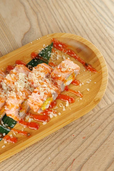 Suşi ruloları taze malzemelerle kaplı ve ahşap bir tabağa baharatlı sos serpiştirilmiş. Gündelik bir ortam, yemekten zevk almak için mükemmel..