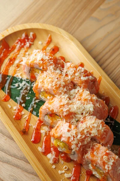 Suşi ruloları ahşap bir tabakta, soslar ve balık pullarıyla kaplı. Yemek alanında besin sunumunu ön plana çıkaran temiz bir tasarım var..