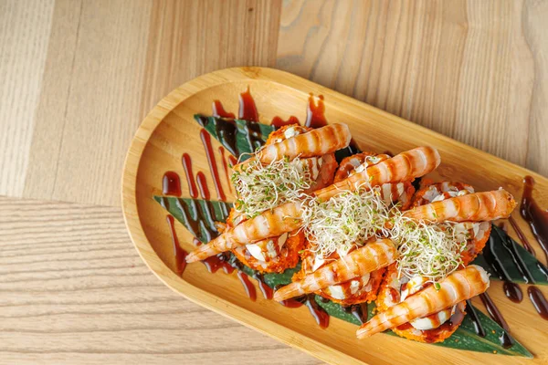 Ahşap tabakta dikkatlice hazırlanmış karides ve lahanalarla süslenmiş suşi, yanında çiselemeli sos ve yeşil sebzeler, Japon mutfağı sergileniyor..