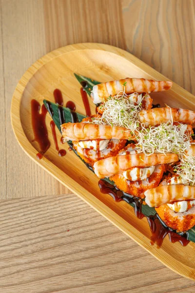 Ahşap tabakta güzel düzenlenmiş ızgara izleriyle birlikte deniz ürünleri ruloları var. Tabak lahanalarla süslenmiş ve sosla ıslatılmış. Bu yemek aşçılık geleneklerinin bir karışımını gözler önüne seriyor..