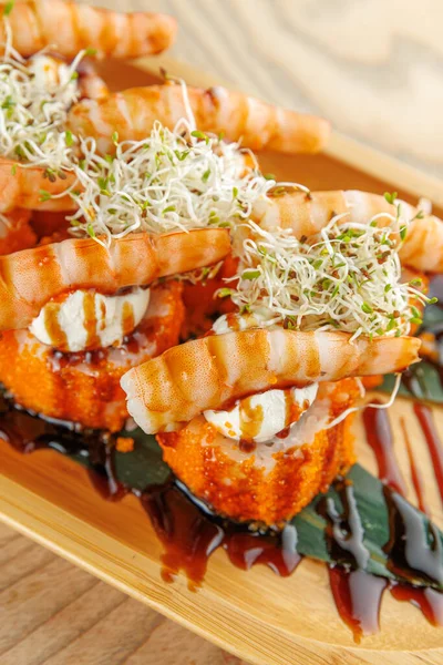 Çıtır karides ve taze lahanayla kaplı karidesli suşi ruloları ahşap bir tabakta oturur. Bir tutam sos, canlı bir restoranda sunumu güçlendirir..