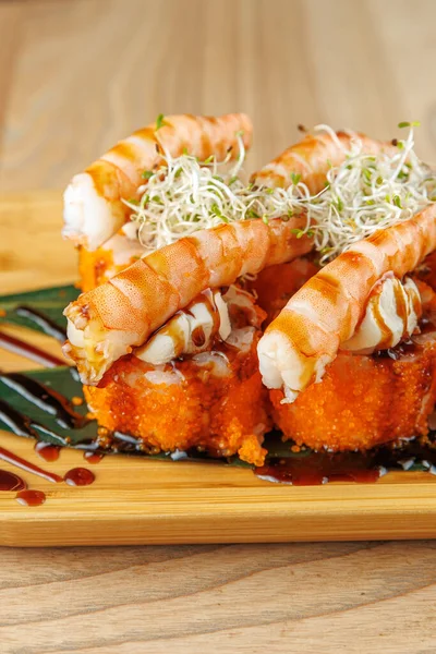 Karidesli suşi ruloları ahşap bir tabakta güzelce düzenlenir. Tabakta parlak bir sos ve taze garnitür var. Japon mutfağının karmaşık hazırlıklarının altını çiziyor..