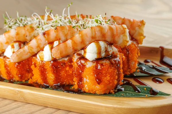 Karides ve tobiko suşi ruloları ahşap bir tabakta, lahanalarla kaplı ve sosla sergileniyor. Bu yemek, deniz ürünleri aşıkları için mükemmel..