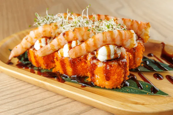 Karides suşi ruloları ahşap bir tabakta sergilenir. Ekmekler sos ve lahanayla kaplı. Bu yemek, modern bir restoranda sunulan yemeğin bir parçasıdır..