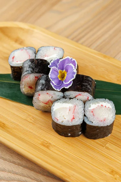 Yengeç ve krem peynirle dolu suşi ruloları ahşap bir tabakta düzenlenir. Mor bir çiçek suşinin üzerinde oturur. Odak noktası yemeğin ayrıntıları ve sunumu..