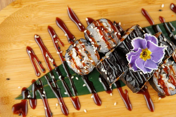 Suşi ruloları bambu tabakta güzelce düzenlenir. Yemek çeşitli malzemeler içeriyor, sosla ıslatılmış ve sunum için bir çiçekle süslenmiş..