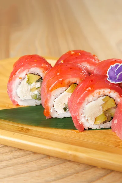 Balık ve sebzeli taze suşi ruloları ahşap bir tabakta düzgünce düzenlenir. Ayarlama, yemek sırasında yemeğin canlı renklerini ve sunumunu vurgular.