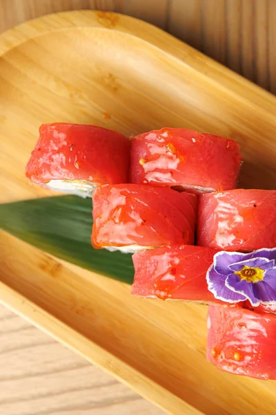 Taze malzemelerle yapılan lezzetli suşi ruloları ahşap bir tabakta güzelce düzenlenir. Canlı bir çiçek sunuma renk katar ve davetkar bir yemek yaratır..