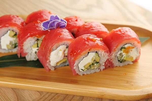 Suşi börekleri ahşap bir tabakta oturur ve pirince sarılmış taze malzemeler sergiler. Sunumda canlı renkler ve çiçekli bir garnitür yer alıyor..