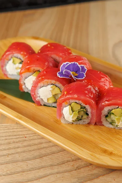 Avokado ve krem peynirle dolu suşi ruloları taze balıkla kaplanır ve çiçekle süslenir. Bu yemek Japon mutfağını temsil ediyor ve canlı tatlar sunuyor..