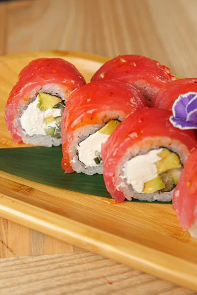 Taze balık ve krem peynirle kaplı suşi ruloları ahşap bir tabakta güzelce oturur. Ayarlar, yerel bir lokantada yemeğin basit sunumunu vurgular.