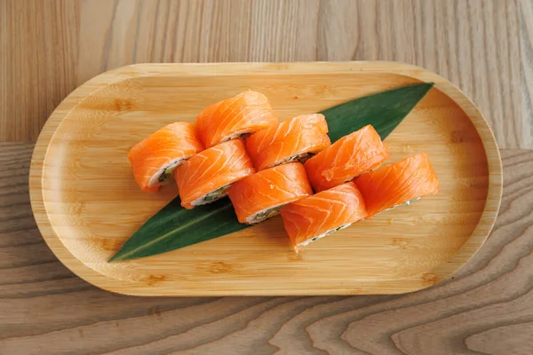 Somon ve pirinçle doldurulmuş suşi ruloları, yeşil bir yaprağa yerleştirilmiş. Dekoru ahşap olan modern bir restoran..