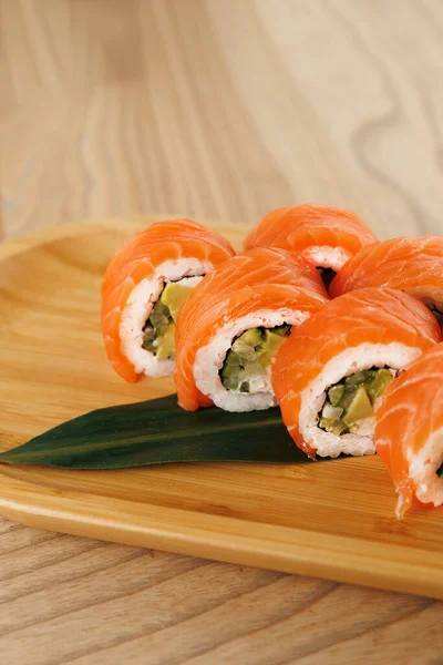 Ahşap tabakta avokado dolu suşi ruloları ve taze somona sarılmış. Yemek, sıradan bir yemek salonunda yemek için hazırlandı..