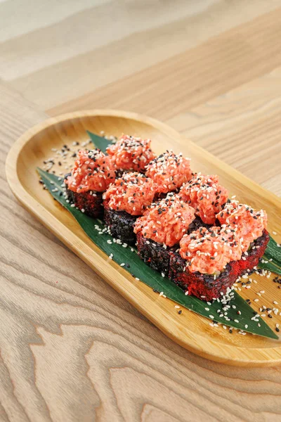 Deniz ürünleri ve pirinçle dolu suşi ruloları bir yaprak üzerinde güzelce düzenlenir ve ahşap bir tabakta servis edilir. Tabak, basit bir ahşap masa ile yemek yerinde eğlenmeye hazır..