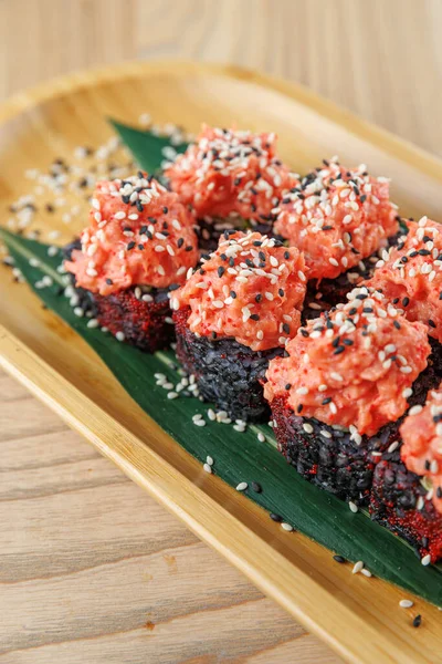 Suşi ahşap bir tabakta servis edilir. Somonla kaplanmış ve susam tohumlarıyla süslenmiş siyah pirinç yer alıyor. Tabakta taze malzemelerle Japon mutfağı sergileniyor..