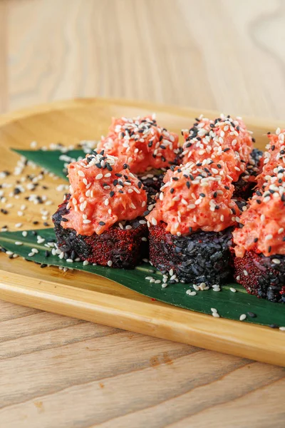 Taze suşi ruloları yeşil yapraklı ahşap bir tabakta sunulur. Ekmeğin üzerine baharatlı somon ve susam tohumları serpiştirilmiş..